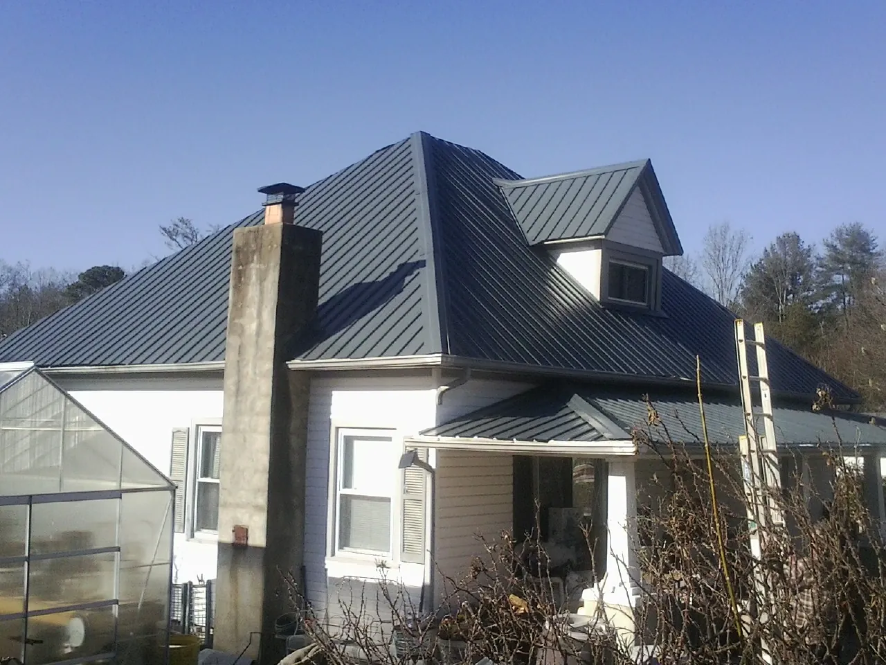 Dark blue standing seam metal roof on a white farmhouse with dormer — Slate & Tile Roof Repair by Roofing Brothers in Crownsville