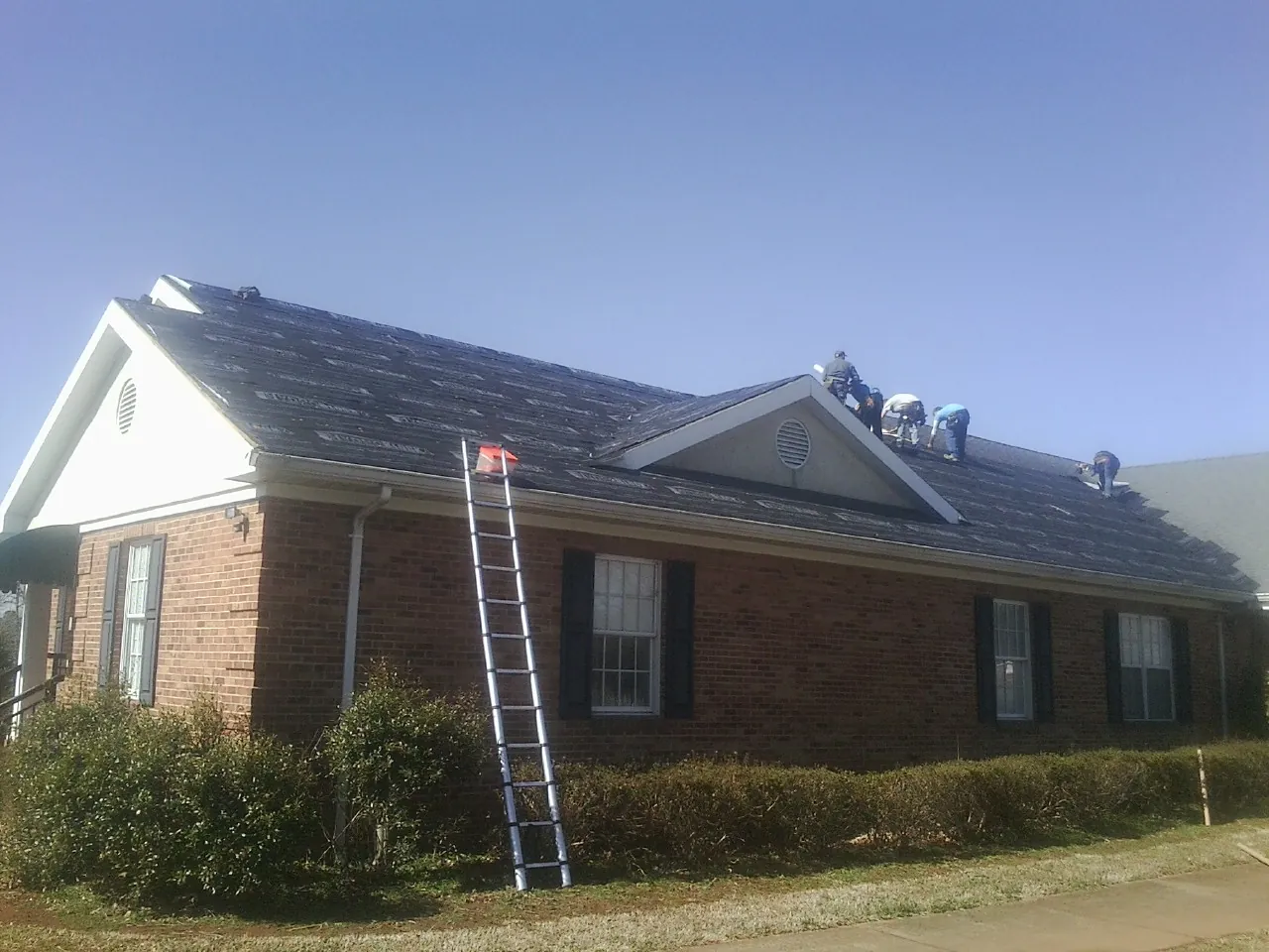Crew tearing shingles off a brick ranch roof with a ladder set — Emergency Roof Repair work by our crew in Crownsville