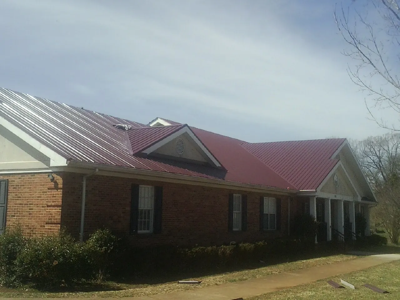 Red metal roof with gabled entries on a long brick building, from a Hail Damage Roof Repair job in Crownsville