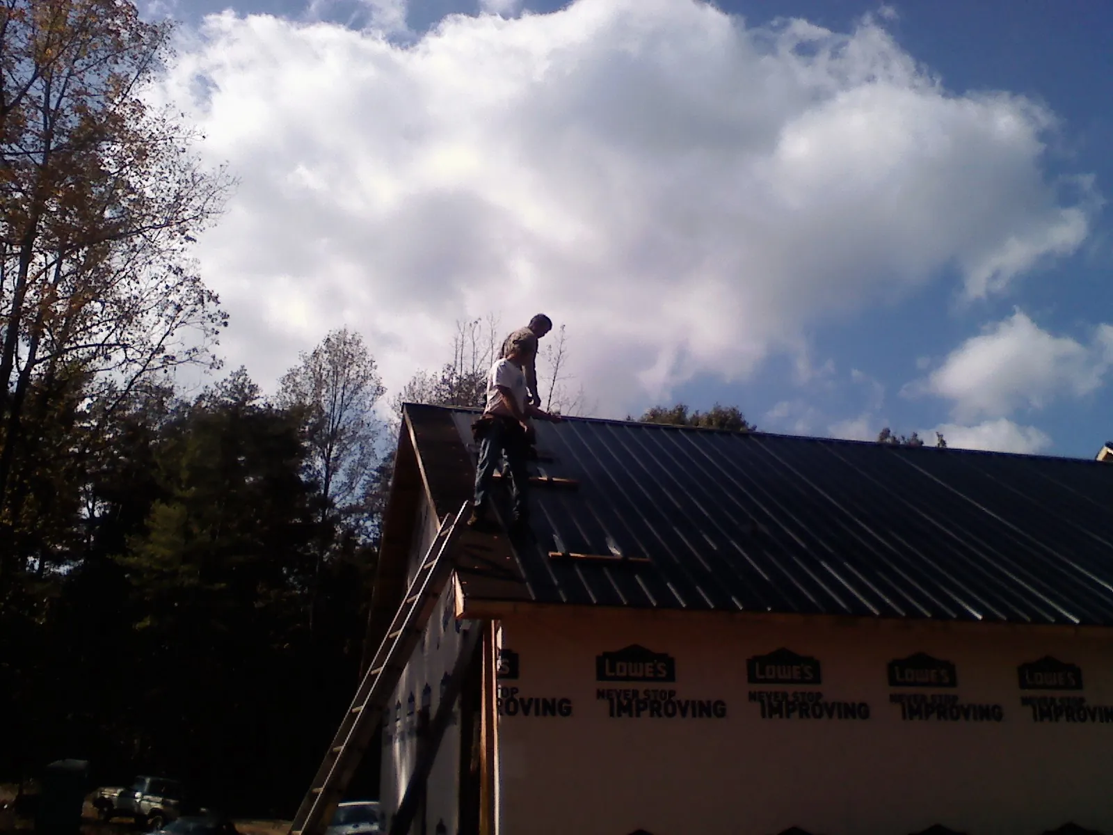 Roofer fastening dark metal panels high against a cloudy sky, from a Roof Inspection job in Crownsville