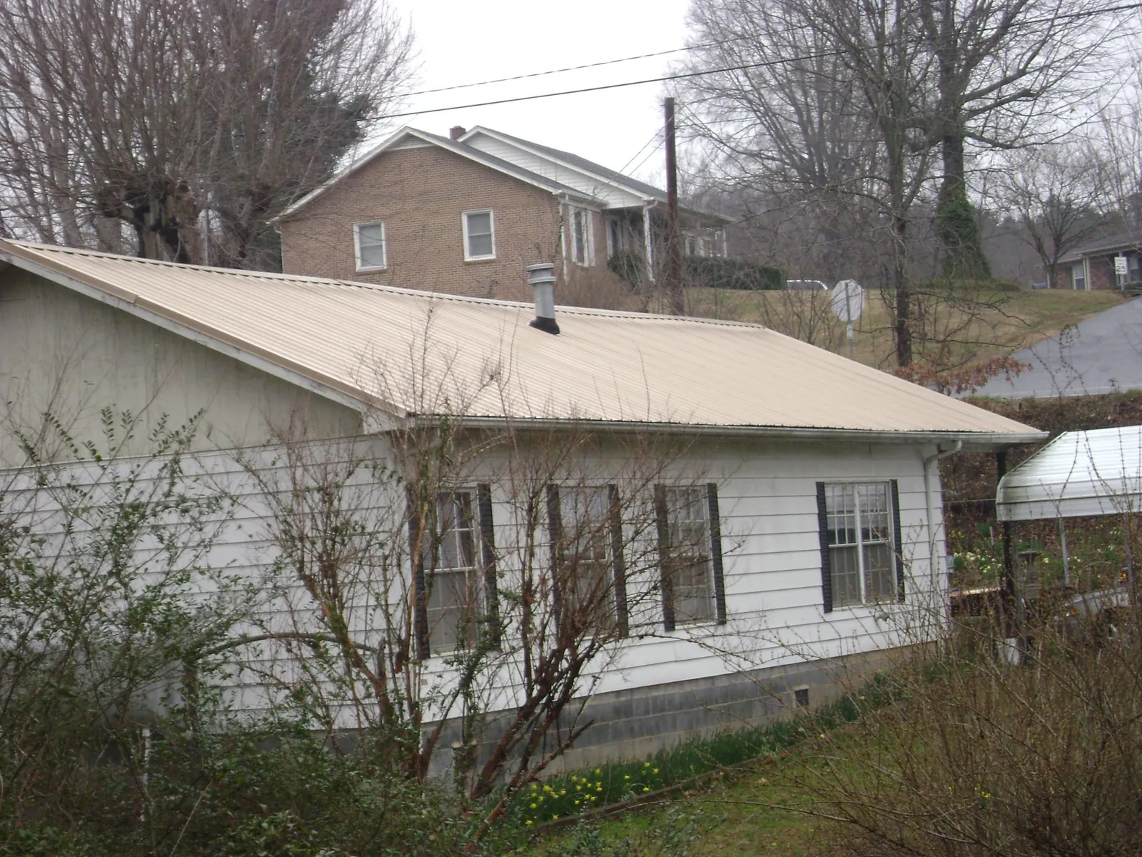 Tan metal roof on a white sided house set into a hillside — Commercial Roofing by Roofing Brothers in Crownsville